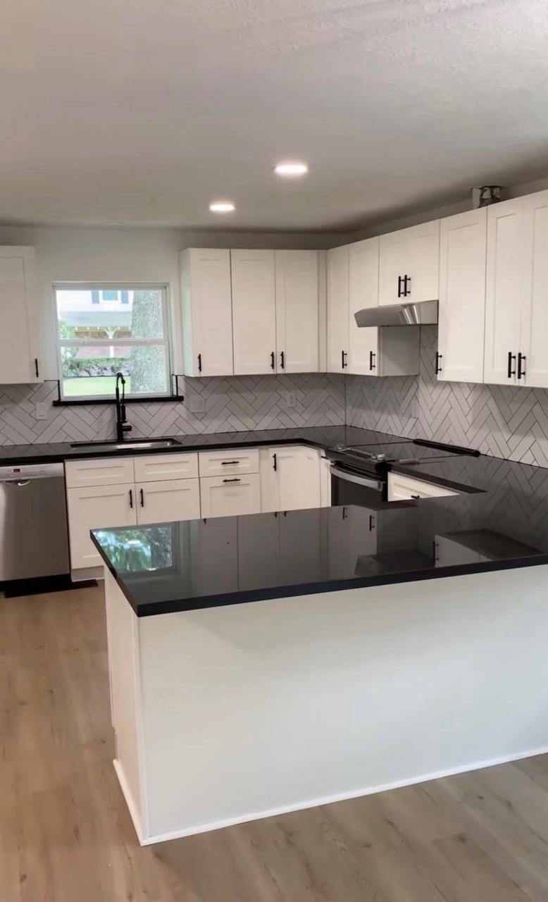 Kitchen renovation after — white shaker cabinets, black counters, herringbone backsplash, island, and recessed lights