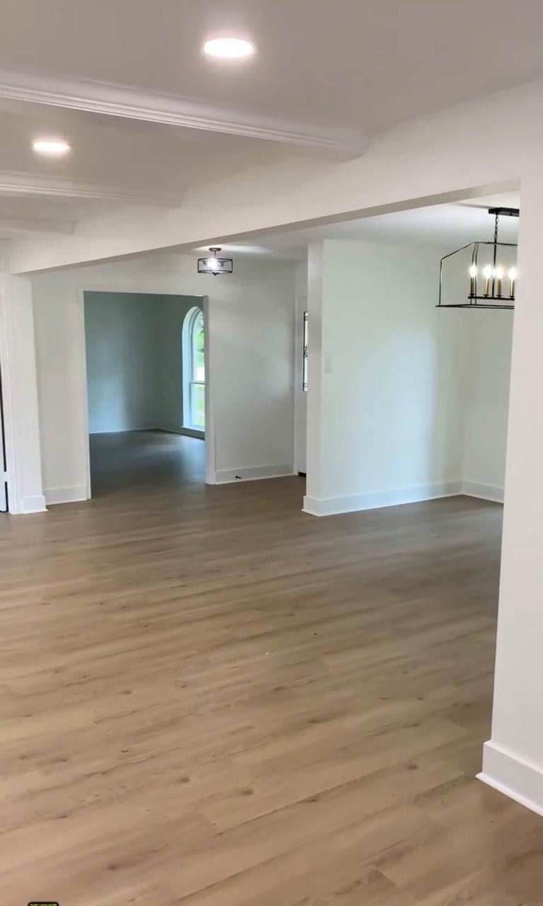Open plan interior after — finished walls, crown molding, recessed lighting, chandelier, and wood-look flooring